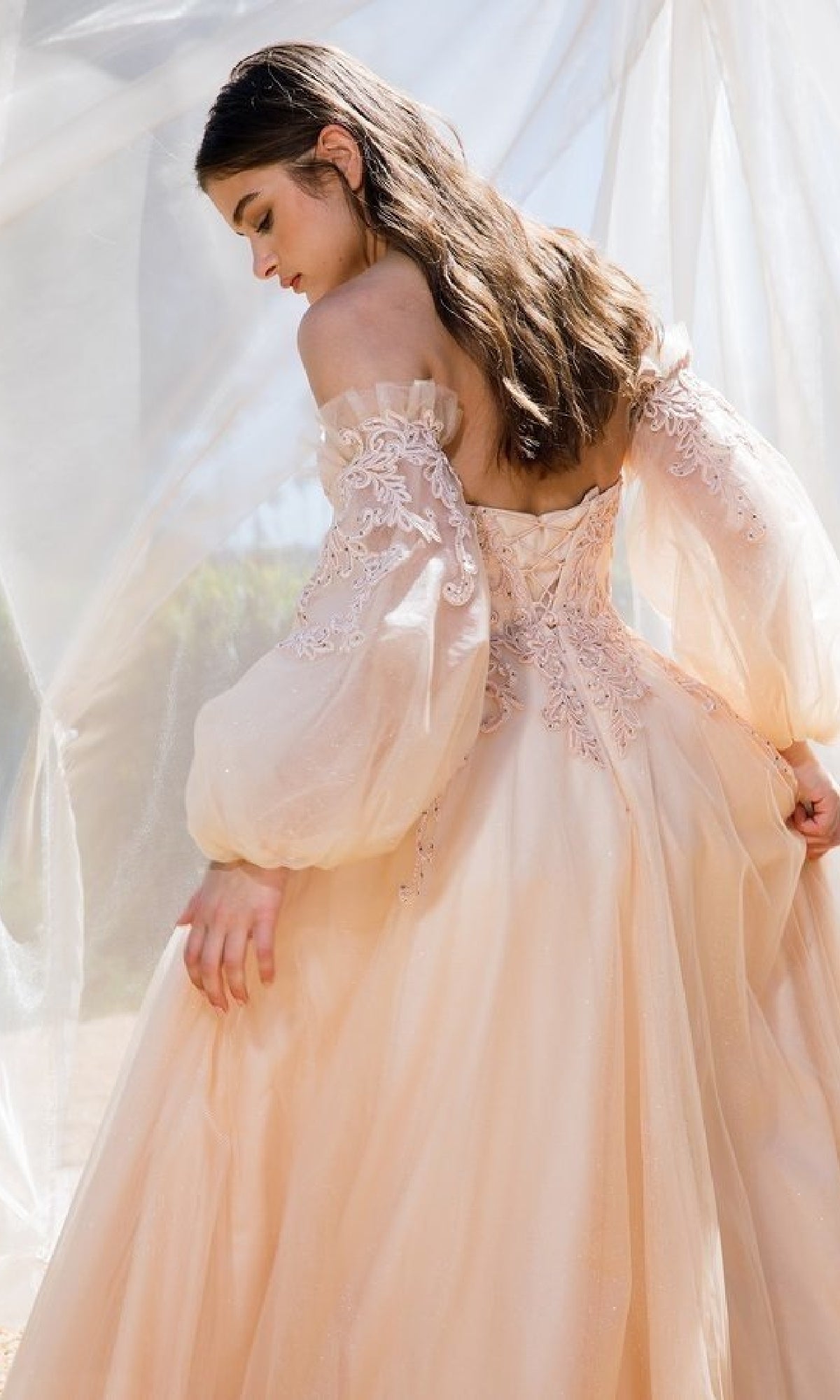 A woman with long brown hair wears the Eureka 9505 Long Sleeve Strapless Long Prom Gown with an embroidered sweetheart bodice and detachable balloon sleeves, set against a soft, translucent background.